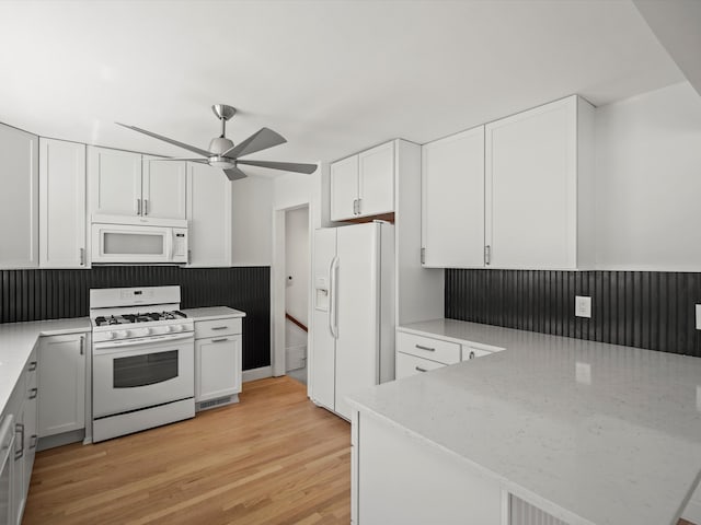 kitchen with a peninsula, a ceiling fan, white cabinets, light wood-type flooring, and white appliances