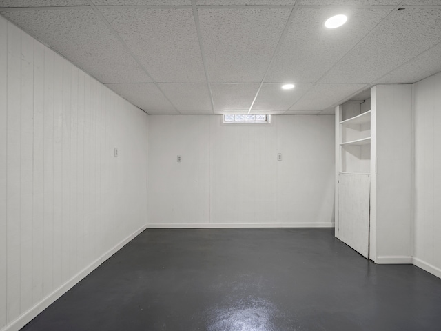 finished basement featuring a drop ceiling, wood walls, baseboards, and recessed lighting