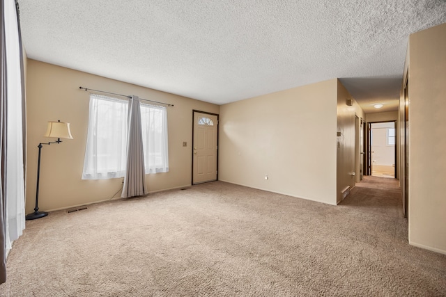 unfurnished living room featuring carpet flooring, plenty of natural light, visible vents, and a textured ceiling