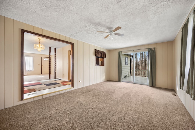 carpeted empty room featuring a textured ceiling, ceiling fan with notable chandelier, and a healthy amount of sunlight