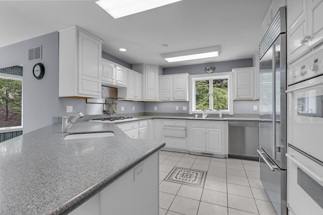 kitchen with a sink, white appliances, white cabinetry, and visible vents