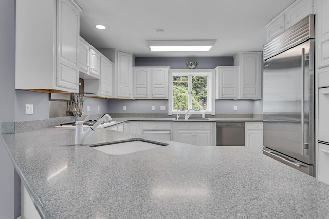 kitchen featuring white cabinetry, appliances with stainless steel finishes, light stone countertops, and a sink