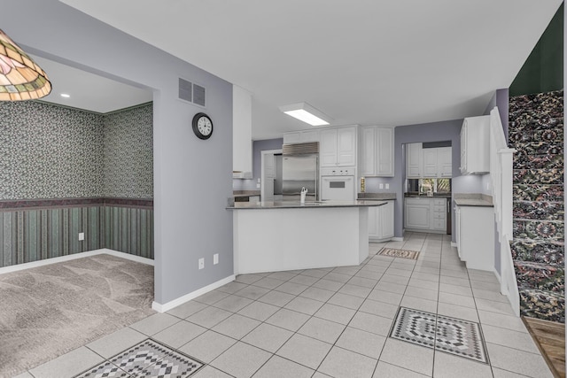 kitchen with wallpapered walls, light tile patterned floors, stainless steel built in fridge, visible vents, and white oven