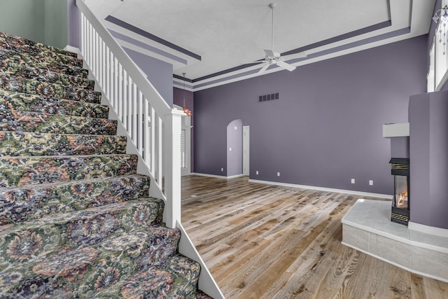 stairs featuring wood finished floors, a high ceiling, a tiled fireplace, visible vents, and ceiling fan