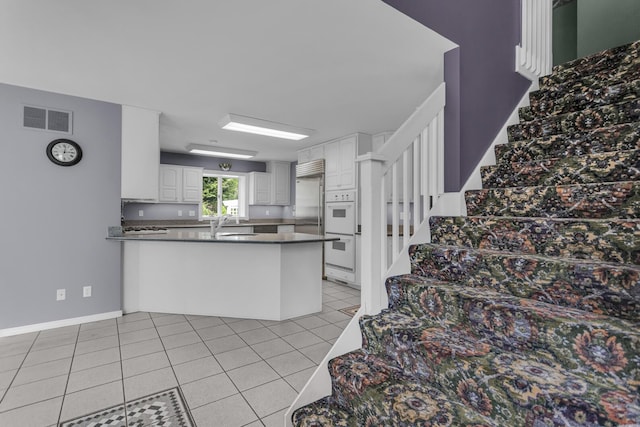 kitchen featuring a peninsula, double oven, visible vents, white cabinets, and dark countertops