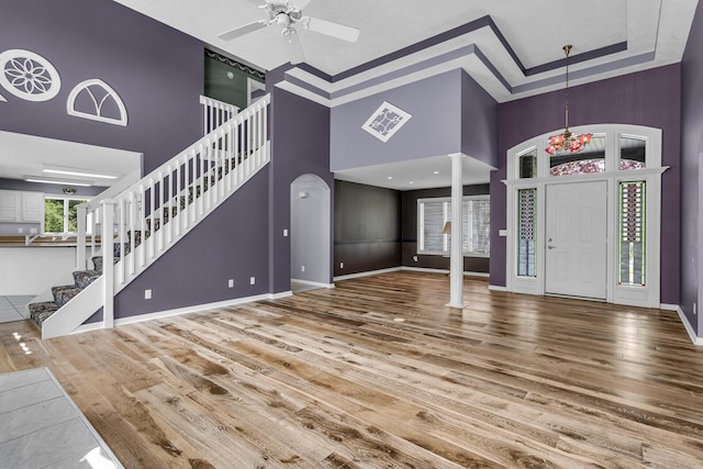 unfurnished living room featuring a ceiling fan, decorative columns, wood finished floors, stairway, and a high ceiling