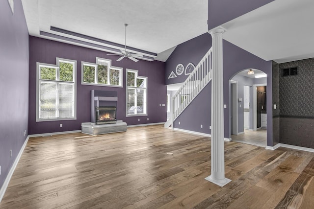 unfurnished living room featuring wood finished floors, a ceiling fan, plenty of natural light, stairway, and a glass covered fireplace