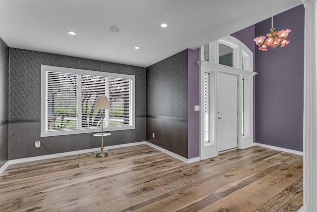 foyer with baseboards, a notable chandelier, wallpapered walls, and wood finished floors