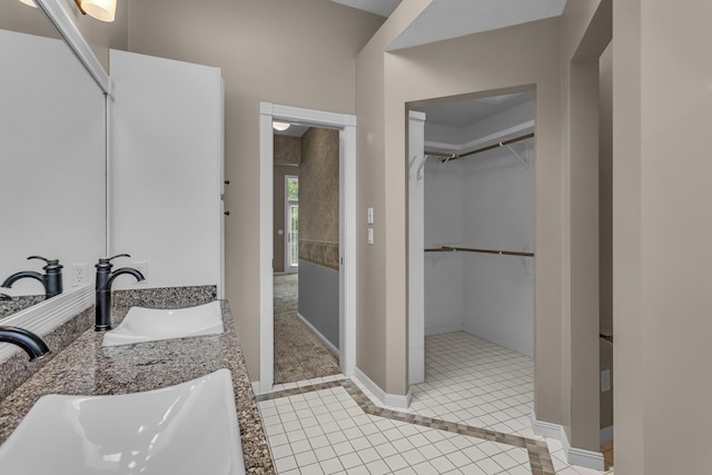 bathroom featuring tile patterned floors, baseboards, a walk in closet, and a sink