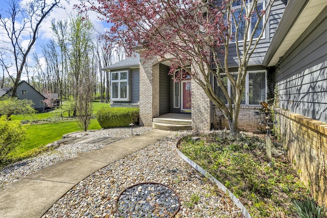 view of exterior entry with a lawn and brick siding