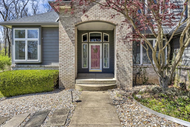 view of exterior entry with roof with shingles and brick siding