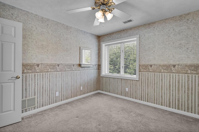 carpeted spare room with wallpapered walls, visible vents, and a ceiling fan
