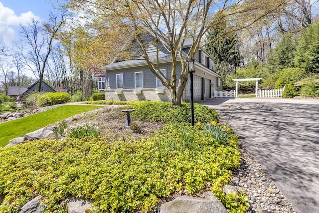 view of side of property with an attached garage, brick siding, fence, and aphalt driveway