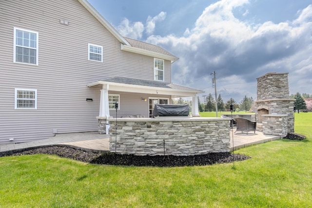 back of property with a patio, a lawn, area for grilling, a stone fireplace, and roof with shingles