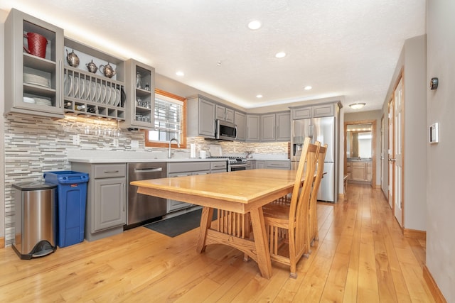 kitchen featuring light wood-style flooring, stainless steel appliances, gray cabinets, light countertops, and decorative backsplash