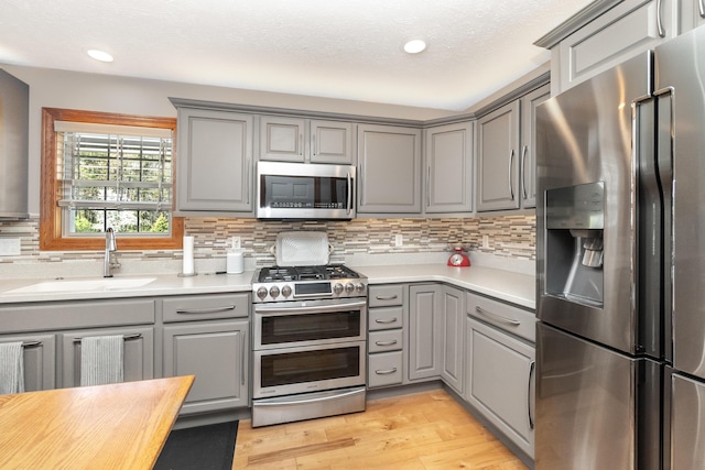 kitchen with a sink, tasteful backsplash, gray cabinets, light wood-type flooring, and appliances with stainless steel finishes