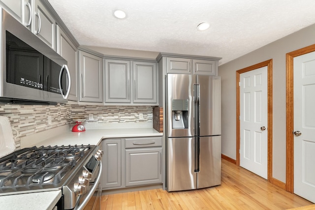 kitchen featuring backsplash, light wood finished floors, appliances with stainless steel finishes, and gray cabinetry