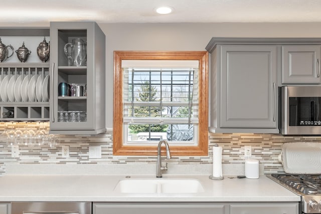 kitchen with a sink, gray cabinetry, backsplash, and appliances with stainless steel finishes