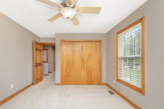 unfurnished bedroom with a closet, light colored carpet, visible vents, ceiling fan, and baseboards