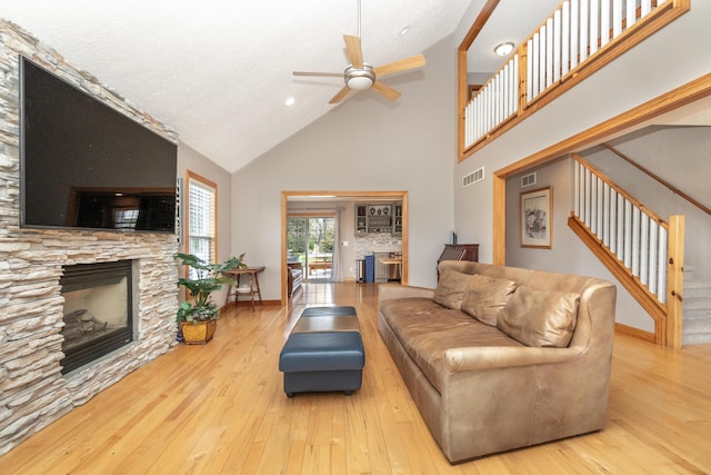living room with hardwood / wood-style floors, high vaulted ceiling, visible vents, a ceiling fan, and a stone fireplace