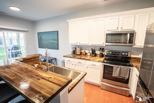 kitchen with wood counters, light wood-type flooring, white cabinetry, and appliances with stainless steel finishes