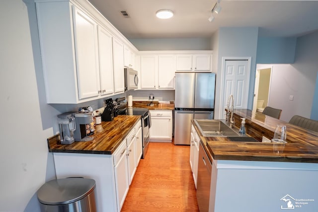 kitchen with light wood finished floors, wooden counters, a sink, appliances with stainless steel finishes, and a kitchen island
