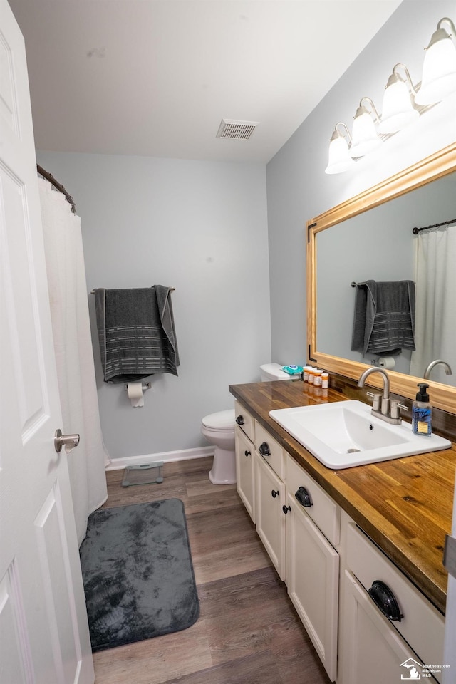 full bathroom with toilet, wood finished floors, vanity, visible vents, and baseboards