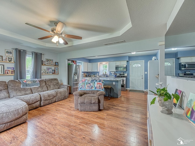 living room with a ceiling fan, wood-type flooring, a textured ceiling, visible vents, and a raised ceiling