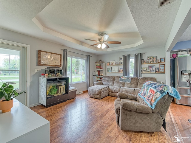 living room featuring a textured ceiling, ceiling fan, light wood-style flooring, a raised ceiling, and baseboards