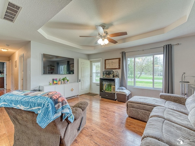 living room featuring a ceiling fan, a textured ceiling, visible vents, a raised ceiling, and light wood-type flooring