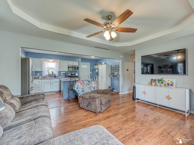 living room featuring light wood-type flooring, visible vents, a raised ceiling, and ceiling fan