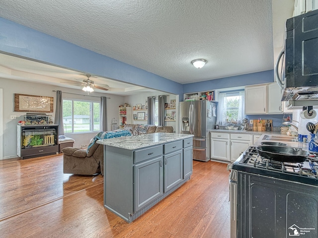kitchen featuring light wood-style flooring, a center island, a sink, black appliances, and white cabinets