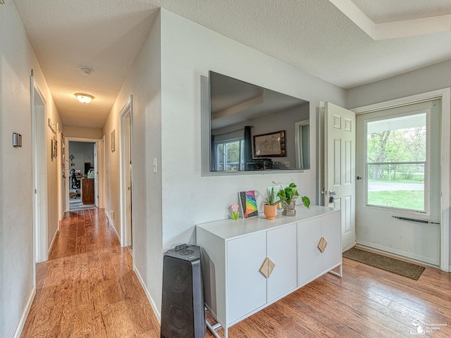 corridor with a textured ceiling, light wood-style flooring, and plenty of natural light