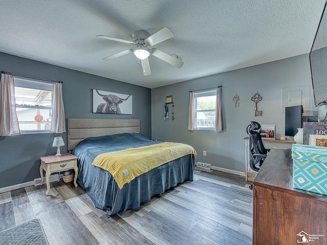 bedroom featuring wood finished floors, a textured ceiling, visible vents, ceiling fan, and baseboards