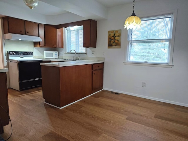kitchen featuring a peninsula, a sink, white microwave, under cabinet range hood, and range with electric stovetop