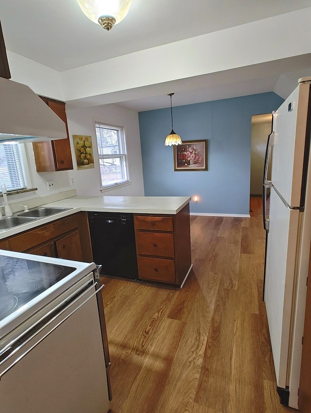 kitchen featuring white appliances, light wood finished floors, a sink, a peninsula, and light countertops