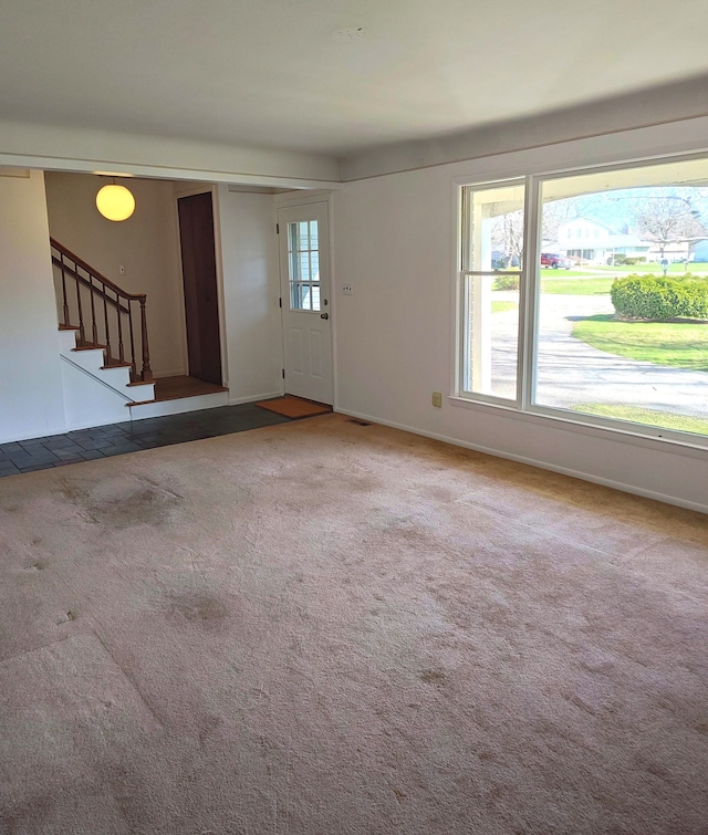 unfurnished living room featuring stairway, carpet floors, and baseboards