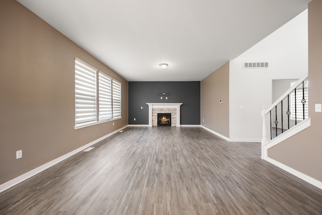 unfurnished living room with wood finished floors, a lit fireplace, visible vents, baseboards, and stairs