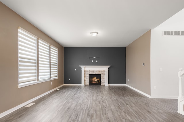 unfurnished living room featuring visible vents, wood finished floors, baseboards, and a stone fireplace