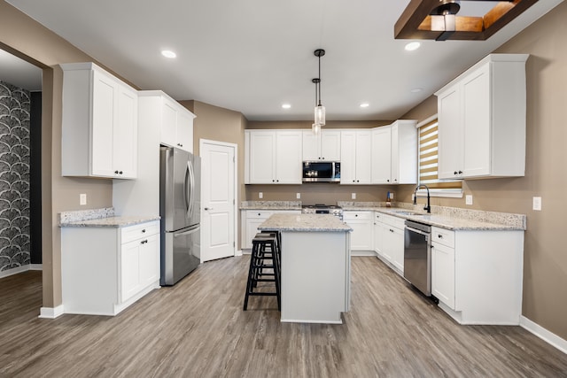 kitchen with a sink, stainless steel appliances, light wood-style flooring, a kitchen island, and baseboards