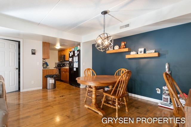 dining area featuring baseboards, a notable chandelier, visible vents, and wood finished floors