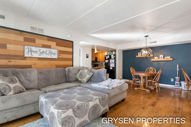 living room featuring visible vents, wooden walls, wood-type flooring, and a notable chandelier