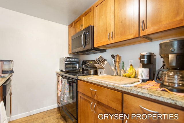 kitchen with stainless steel microwave, brown cabinets, light stone counters, black range with electric cooktop, and light wood-style floors