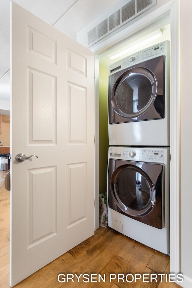 clothes washing area with laundry area, stacked washer and clothes dryer, visible vents, and wood finished floors