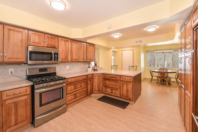 4780 Dutcher Rd, Howell, MI 48843 - kitchen with a peninsula, brown cabinetry, backsplash, and appliances with stainless steel finishes
