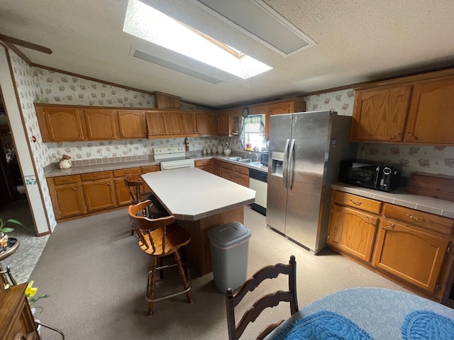 kitchen featuring white appliances, wallpapered walls, lofted ceiling, a sink, and brown cabinets