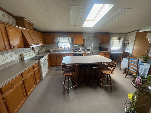 kitchen with stainless steel fridge with ice dispenser, electric stove, wallpapered walls, brown cabinetry, and a breakfast bar area