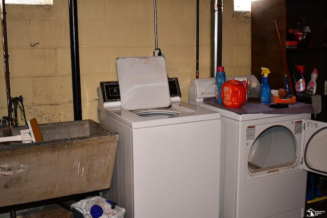 laundry area with washing machine and clothes dryer, a sink, and concrete block wall