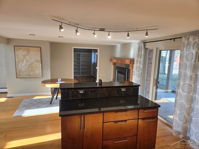 8570 Hornbeam Ln, Saginaw, MI 48603 - kitchen featuring light wood finished floors, rail lighting, baseboards, a tile fireplace, and dark stone counters