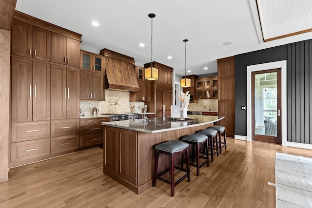 5744 Wyndam Ln, Brighton, MI 48116 - kitchen featuring a kitchen island with sink, decorative backsplash, light wood-style flooring, and custom exhaust hood